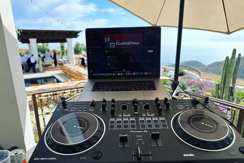 Pioneer DDJ-REV1 controller and MacBook running Spotify Cocktail-hour playlist on a coastal patio.