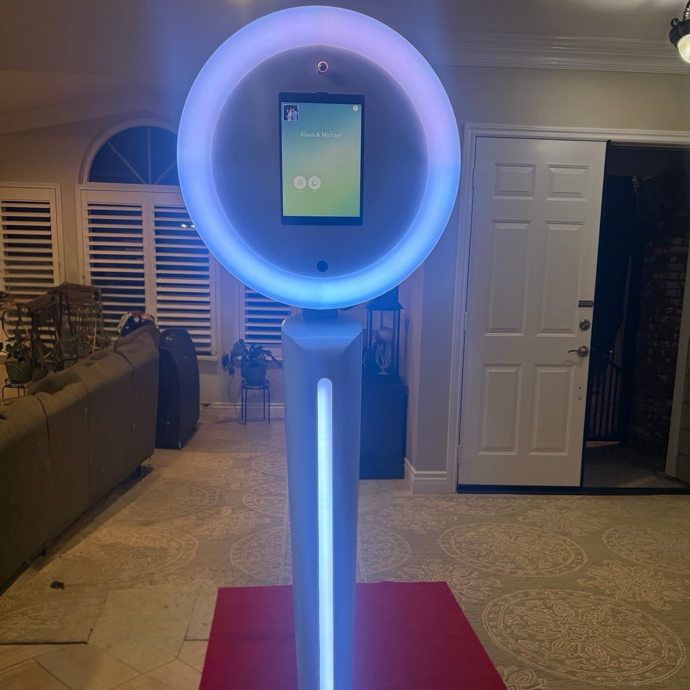 Tall white ring-light selfie photo booth with iPad screen lit blue on a red platform.