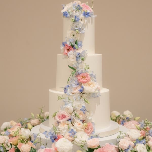 Three-tier white wedding cake with cascading blue, pink, and white florals