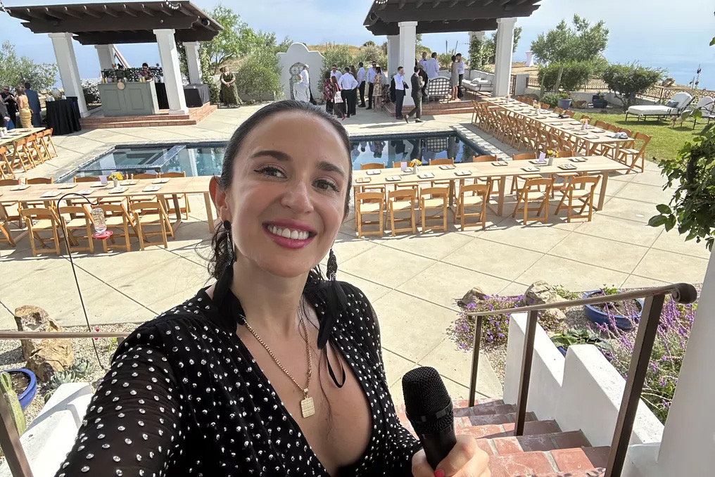 Jackie at the top of the staircase overlooking a pool-side wedding setup with chairs, tables, and ocean view.